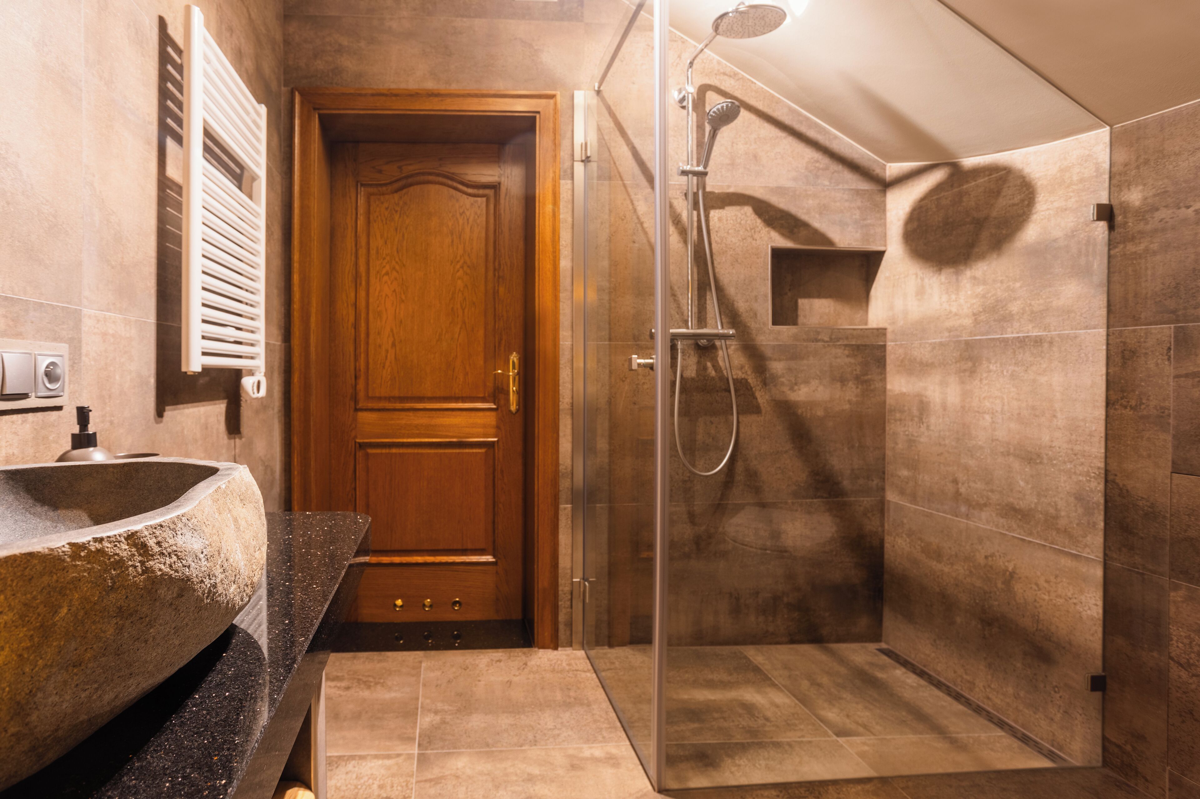 A bathroom with a stone sink, wooden door, and a glass-enclosed shower area.