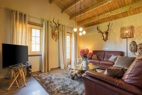A living room with a leather sofa, a glass coffee table, a flat-screen TV, and a rustic decor including antler wall art.