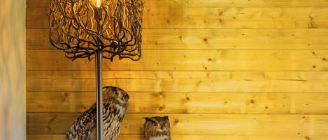 A cozy room with a wooden wall, two mounted owls, a brown leather sofa, and a unique light fixture.