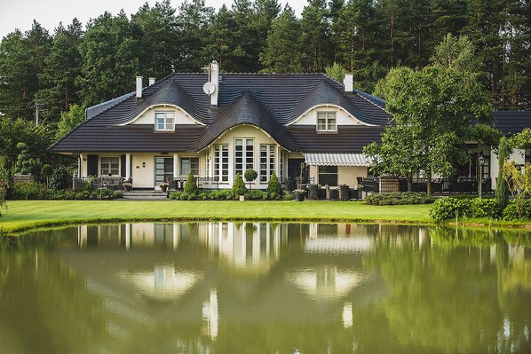 A large, two-story building with a symmetrical facade, a central entrance, and a reflection in a calm pond. - Dwór Myśliwski Hubertus  (gmina Lubniany)