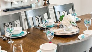 Un coin repas avec une table en bois dressée pour quatre personnes, entourée de chaises. On peut voir une sculpture de poisson au mur, une plante en pot et des œuvres d’art encadrées.