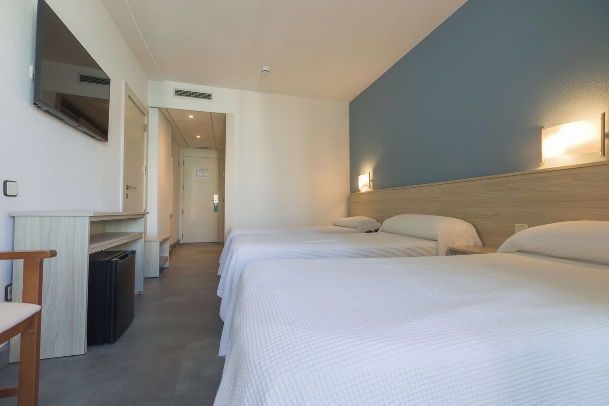 A hotel room with two beds, a desk, and a small trash bin.