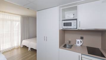 A compact hotel room with a kitchenette, a bed, and a window with curtains.