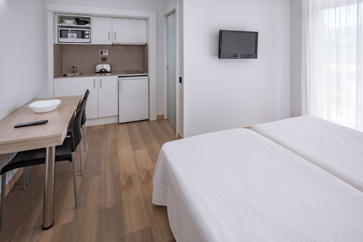 Habitación de hotel compacta con kitchenette, cama, televisor y zona de comedor.