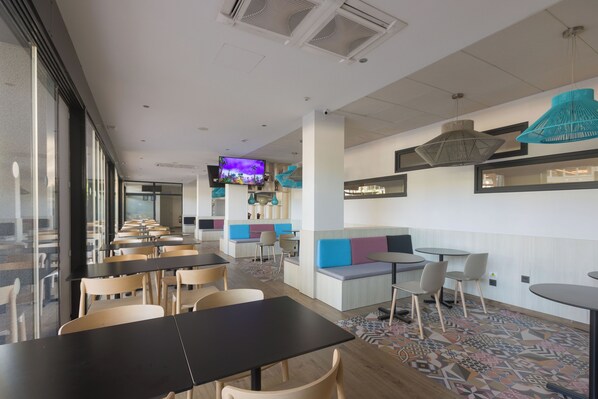 A modern restaurant with high tables and booths, a TV screen, and a patterned floor. - Ponient Aparthotel Marinada by PortAventura World (Salou)
