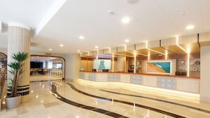 A hotel reception area with a curved reception desk, a large TV screen, and a potted plant. - Ponient Aparthotel Marinada by PortAventura World (Salou)