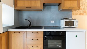Een kleine keuken met houten kastjes, een zwart fornuis, een witte magnetron en een witte koelkast.