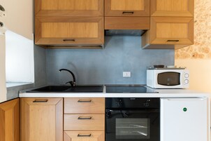 Una cocina compacta con armarios de madera, estufa negra, microondas blanco y refrigerador blanco.