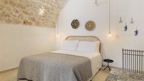 Een slaapkamer met een stenen muur, een bed met een grijze sprei, twee decoratieve borden aan de muur, en een klein tafeltje met een zwart dienblad.