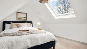 A bedroom with a bed, a nightstand, a lamp, a picture on the wall, and a skylight. - Luxury 2 Bedroom Cottage, with private courtyard and garden. (Killin)