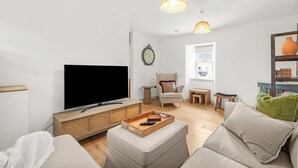 A modern living room with a flat-screen TV, wooden cabinet, ottoman, and a green cushion on a sofa. - Luxury 2 Bedroom Cottage, with private courtyard and garden. (Killin)
