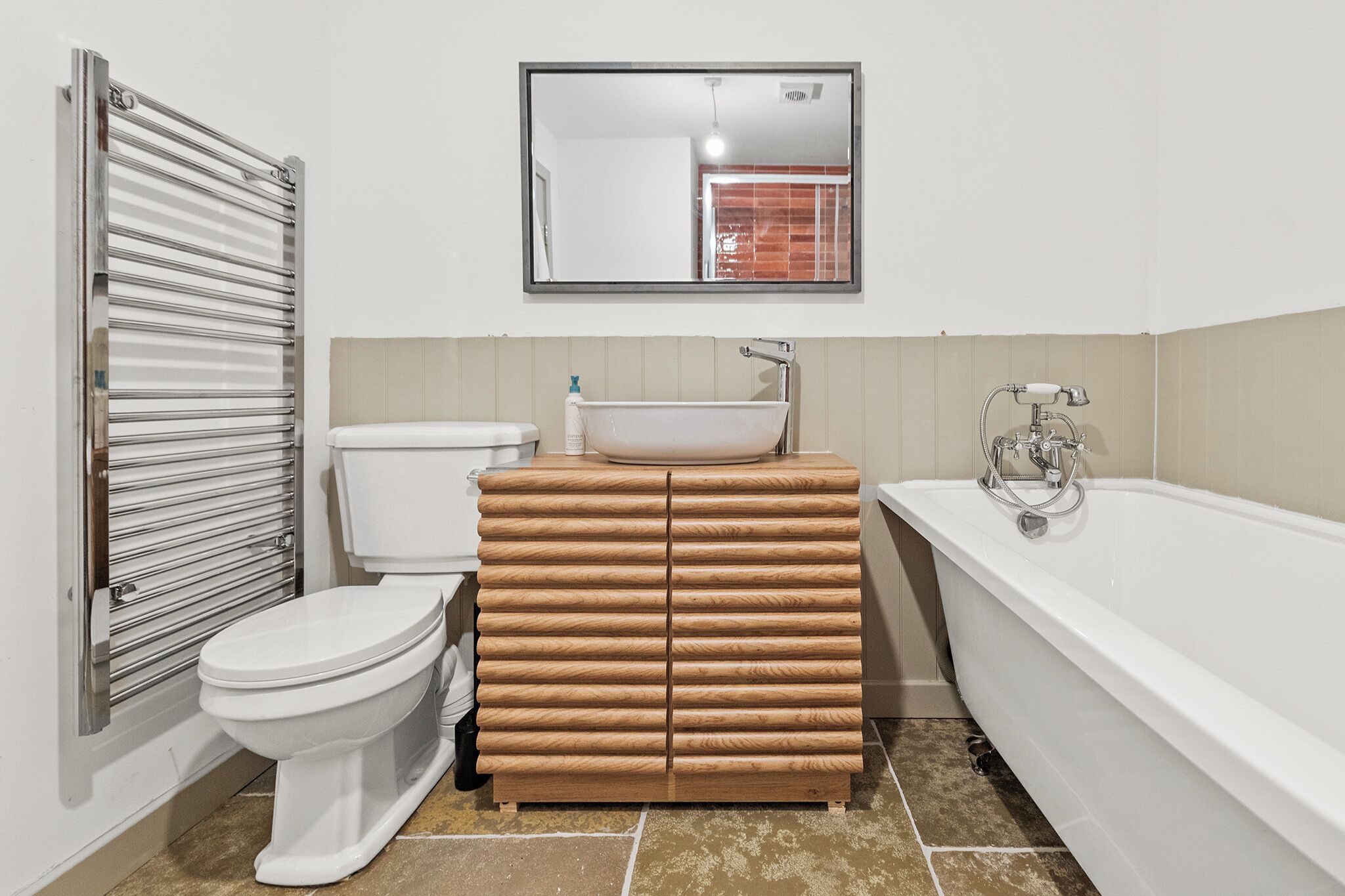 Un baño con inodoro, tocador de madera con lavamanos y bañera.