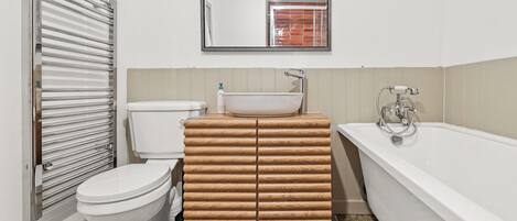 Un baño con inodoro, tocador de madera con lavamanos y bañera.