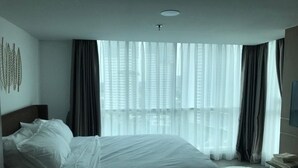 Ein modernes Hotelzimmer mit einem großen Bett, einem runden Teppich und Blick auf die Stadt durch transparente Vorhänge.