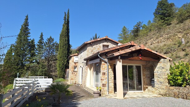 Una casa de piedra con techo de tejas, camino de grava y valla de madera.