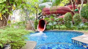 Ein Pool mit Wasserrutsche, umgeben von üppiger Vegetation und Palmen.