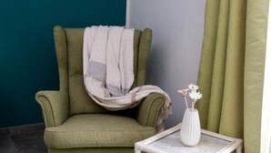 A room with a green armchair, a small table with a white vase, and a teal wall.