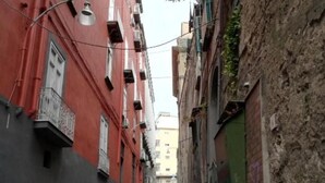 A narrow alleyway between buildings with balconies and a street lamp.