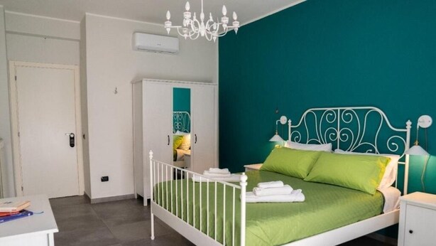 A bedroom with a white metal bed frame, green bedding, a white nightstand, and a teal accent wall.