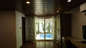A room with wooden flooring, a sliding glass door leading to a balcony, and a TV on the right wall.
