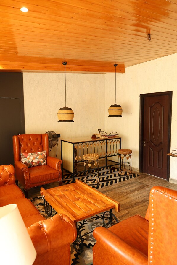 Una habitación con sillones de cuero, una mesa de centro de madera, una alfombra estampada y un techo de madera.