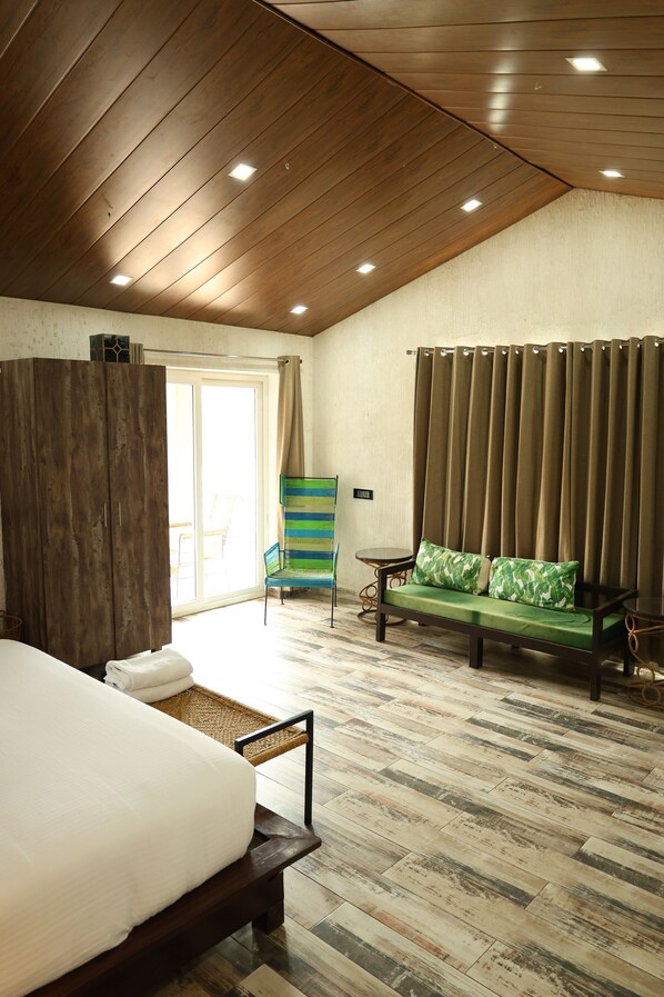Un dormitorio con cama, un armario de madera, un sofá verde con cojines, una mesita y una silla.