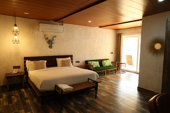 A well-lit bedroom with a large bed, a wooden bench, a nightstand, and a green sofa.