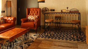 A cozy living room with a wooden ceiling, a leather armchair, a coffee table, and a patterned rug.