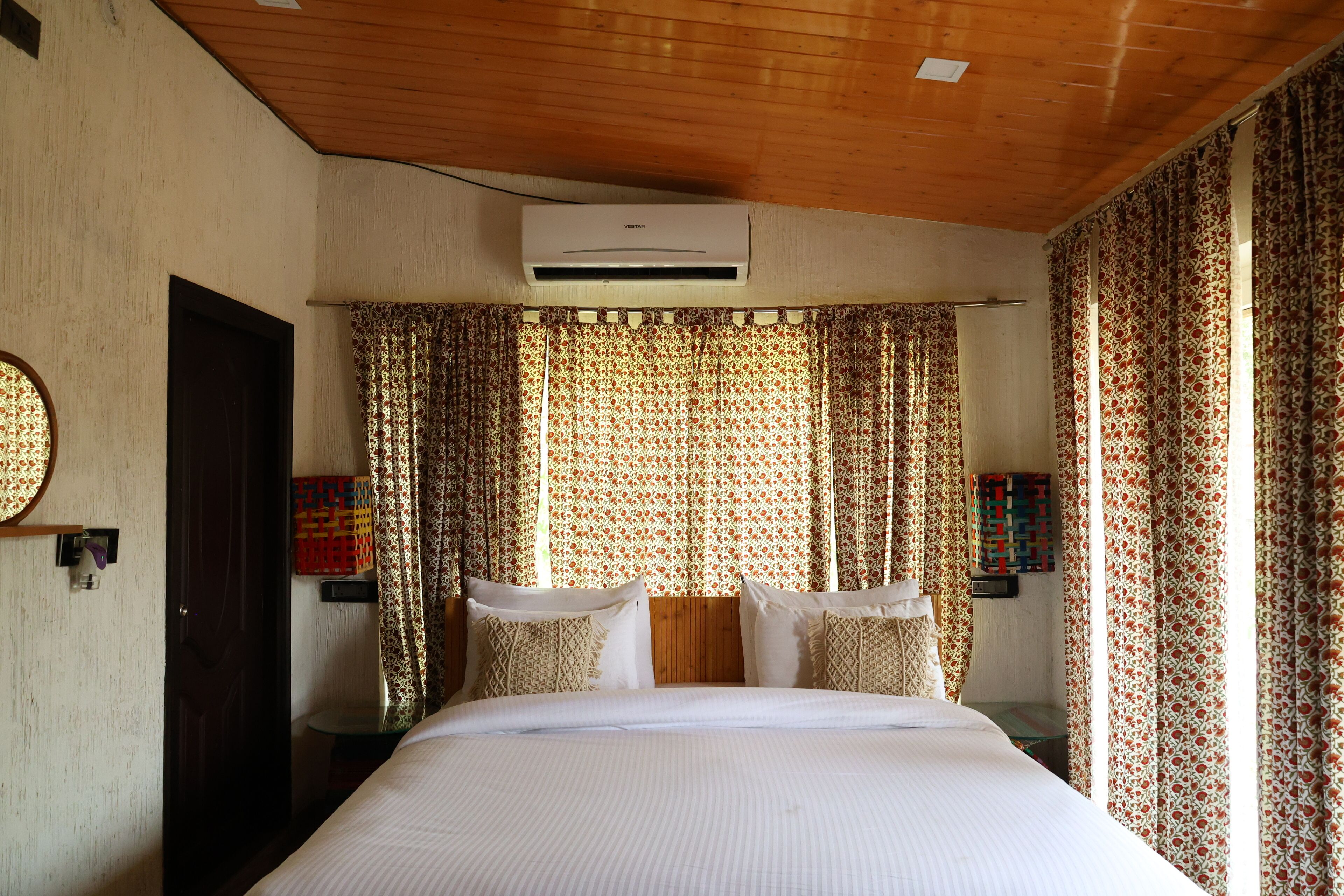 Ein Hotelzimmer mit einem großen Bett, Holzboden, gemusterten Vorhängen und einer Klimaanlage.