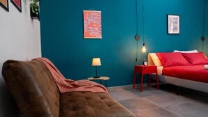 A room with a brown leather armchair, a red bed with matching pillows, a small round table with a lamp, and two framed artworks on teal walls. - B&B MilleCulure: Charming double room with private bathroom  (Napoli)