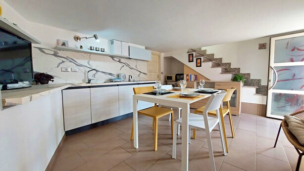 A modern kitchen with a marble backsplash, a dining area with a white table and yellow chairs, and a staircase leading to a loft bedroom. - Talia - Three Bedroom House, Sleeps 4 (Olmedo)