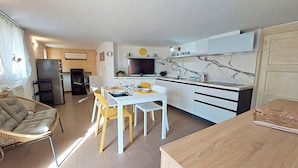 A modern kitchen with white cabinets, a dining area with a white table and yellow chairs, and a large window with curtains. - Talia - Three Bedroom House, Sleeps 4 (Olmedo)