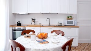 Una cocina compacta con armarios blancos, encimera de madera, un fregadero, cocina y microondas. Hay una mesa con sillas y una cesta de naranjas.