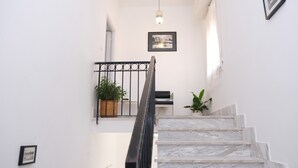 Una escalera con escalones de mármol, barandilla de metal negro y dos plantas en macetas.