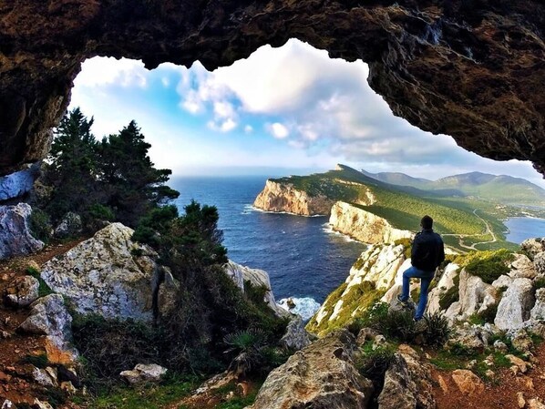 A person sitting on a rocky outcrop overlooking a coastal landscape with a view through a cave opening.