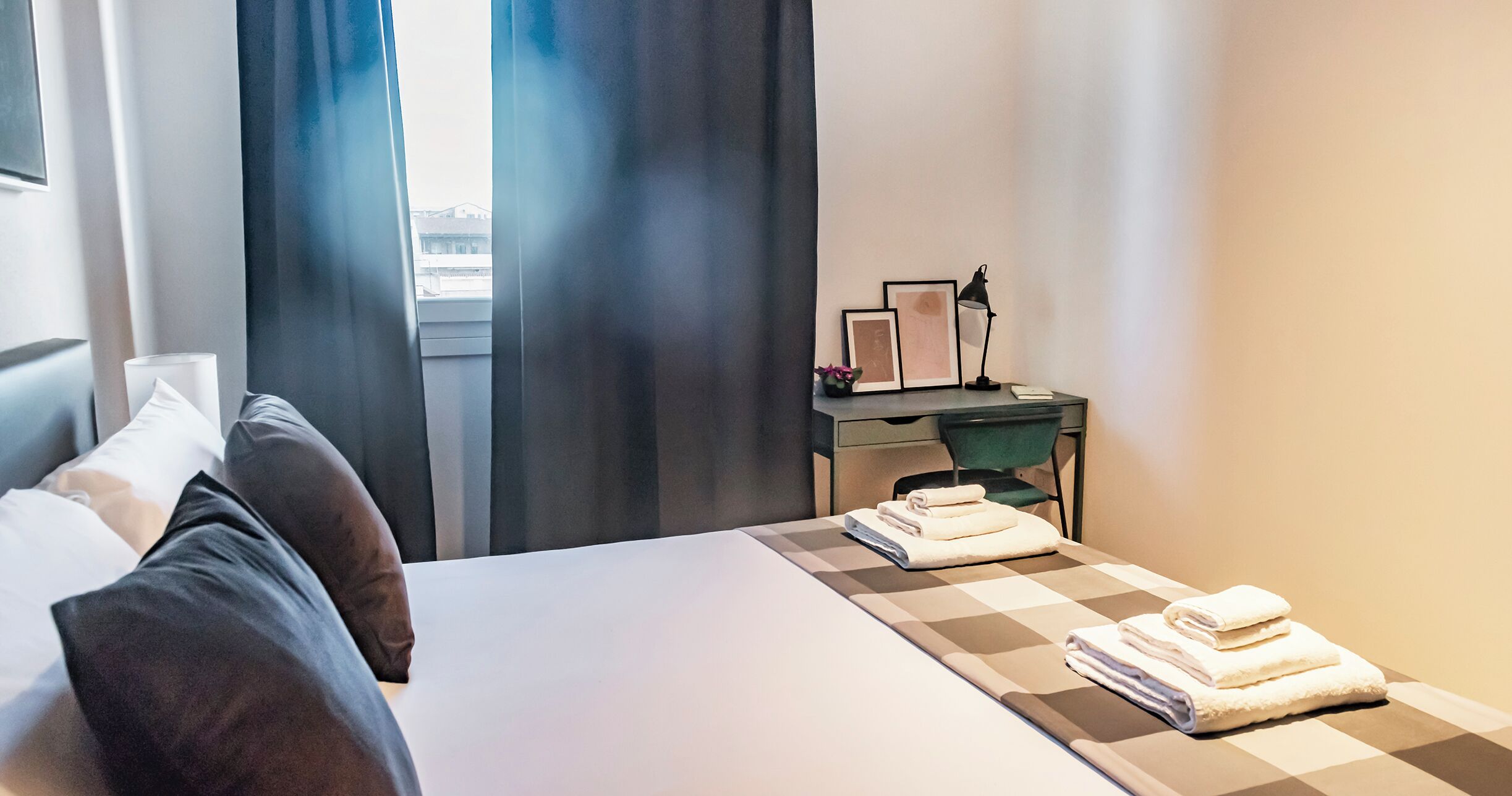 Ein Hotelzimmer mit Bett, Schreibtisch, Stuhl und einem fensterbepflanzten Fenster.