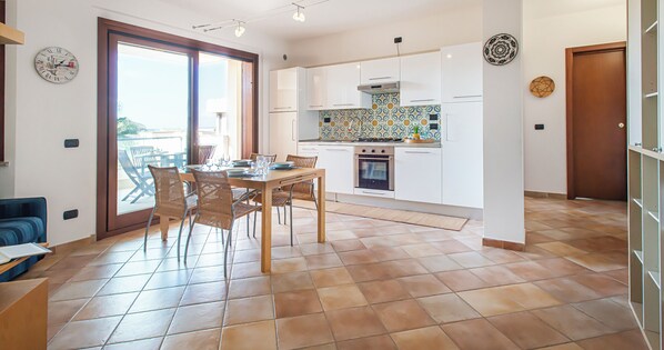 A modern kitchen with white cabinets, a tiled backsplash, and a dining area with a wooden table and wicker chairs.