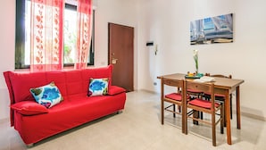 Een rode bank met kleurrijke kussens, een houten eettafel met stoelen, en een schilderij aan de muur.