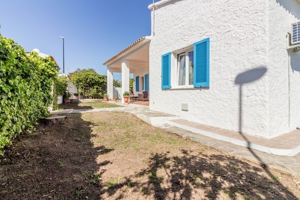 A white building with blue shutters, a covered patio, and a garden area.