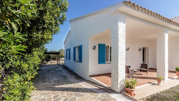 Un bâtiment blanc avec des volets bleus, un chemin de pierre et un patio aménagé avec des chaises et des plantes en pot.