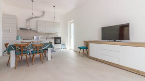 Une cuisine moderne avec des meubles blancs, un coin repas avec des chaises en bois et un téléviseur à écran plat fixé au mur.