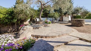 Une terrasse en pierre avec un espace de repos circulaire également en pierre, entouré d’oliviers et de plantes à fleurs.