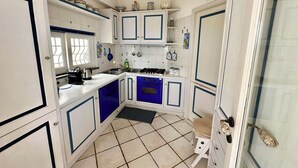A compact kitchen with white cabinets, blue accents, a gas stove, and a small sink.