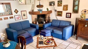 A living room with blue patterned sofas, a wooden coffee table with books and remote controls, and a tiled floor.