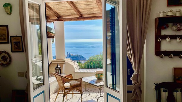 A room with a view of the sea, a wicker chair, a table, and a tiled floor.
