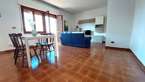 Ein geräumiges Zimmer mit Esstisch und Stühlen, einer Sitzecke und einer Küchenzeile mit Schränken und einem Fernseher.