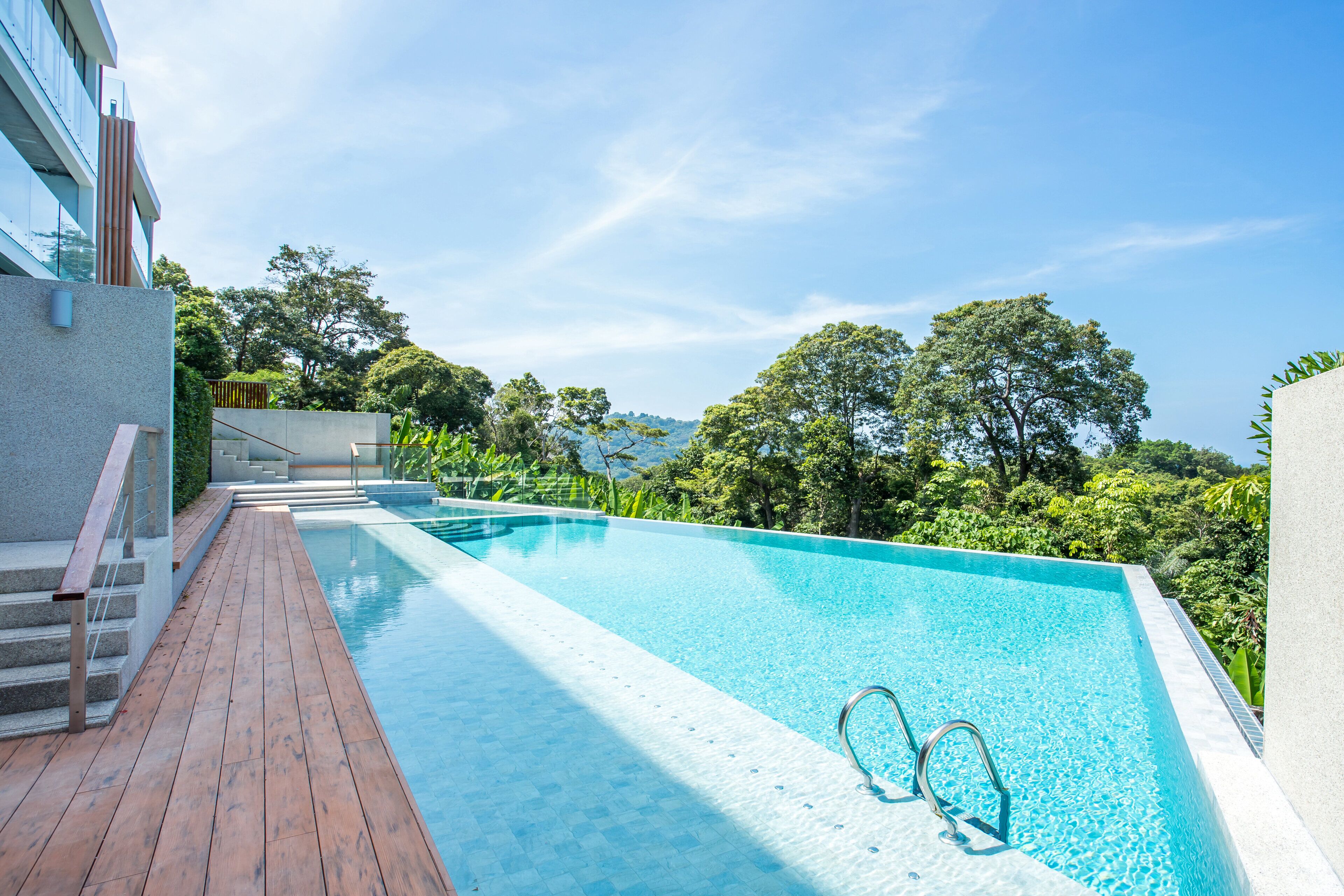 A modern outdoor swimming pool with a wooden deck and a view of lush greenery and distant hills.