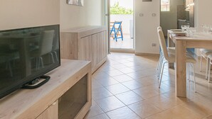 A modern kitchen with a flat-screen TV, wooden cabinets, and a dining area with chairs and a table.