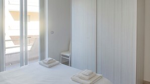 A hotel room with a large window, a bed with two neatly folded towels, and a chair against the wall.