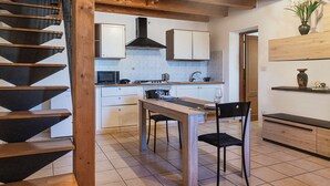 A modern kitchen with a dining area, wooden staircase, and a view of the living area. - Machin 3 - One Bedroom Apartment, Sleeps 2 (Alghero)